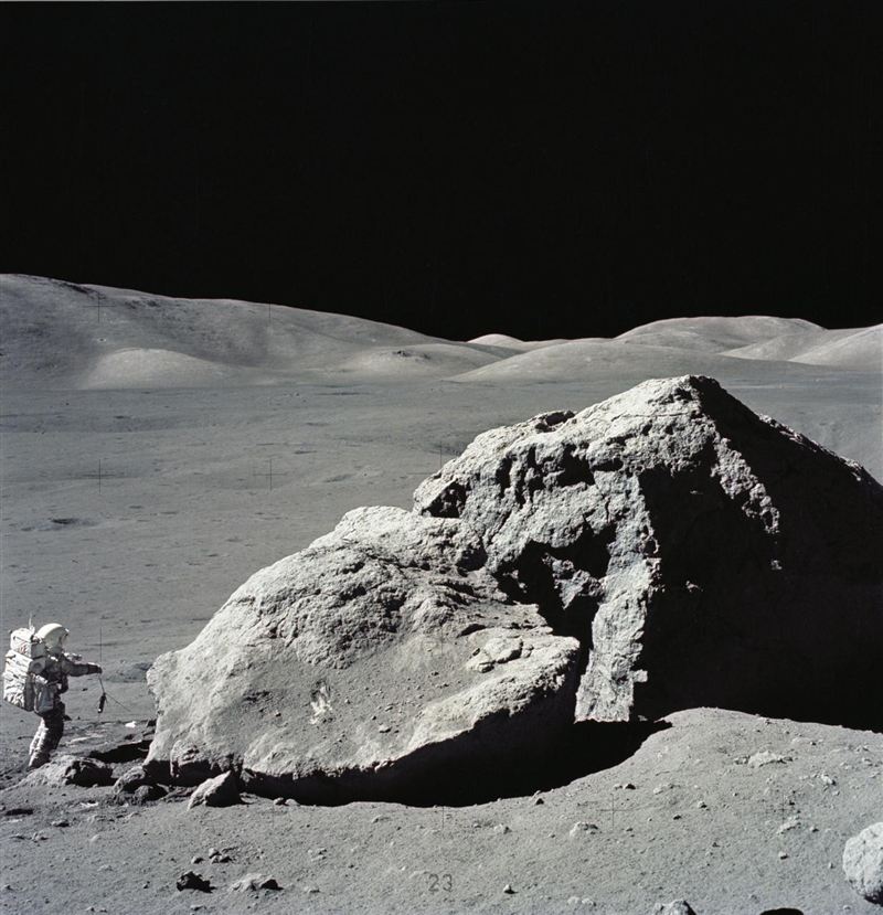 Astronaut Harrison Schmitt beside a large split boulder on the Moon